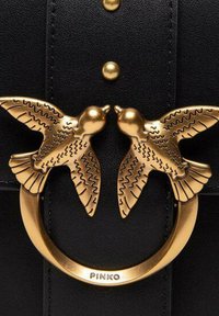 Black leather handbag featuring a gold circular clasp with two intricately detailed birds. Textured accents and gold studs complete the design.