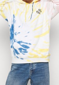 Felpa realizzata in cotone misto, con un motivo tie-dye blu, giallo e rosa su sfondo bianco. Cappuccio regolabile con coulisse.