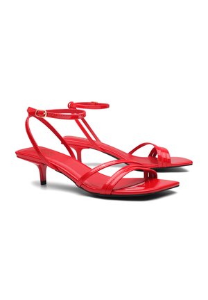 Sandali in pelle patent rossa con cinturini sottili, punta aperta, soletta quadrata e tacco basso. Cinturino alla caviglia regolabile con dettaglio in fibbia dorata.