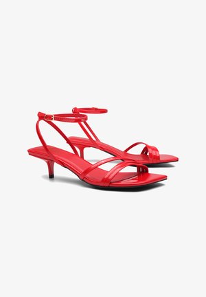 Red patent leather sandals with thin straps, open toe, square footbed, and low heel. Adjustable ankle strap with a gold buckle detail.