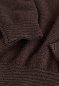Brun stickad tröjfabrikat med strukturerade ribbmönster. Mjuk, något fluffig textur, med kontrasterande släta områden vid muddar.
