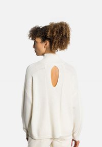 Maglione bianco a maglia con collo alto, taglio oversize e dettaglio a taglio sul retro. Presenta accenti a coste e una texture morbida.