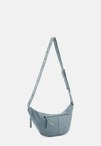 Borsa a tracolla in pelle blu con forma curvata, tracolla regolabile con accessori in metallo e tasca frontale con zip. Texture liscia.