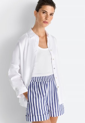 Chemise blanche à boutons, superposée à un débardeur blanc, assortie à un short à rayures bleues et blanches. Tissu doux, coupe décontractée et manches retroussées.