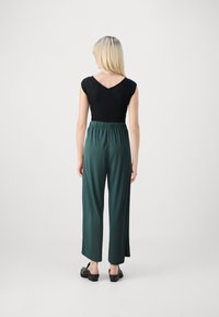 Haut noir ajusté avec des manches à volant et un dos en V, associé à un pantalon large vert. Tissu lisse et détail de taille élastique à noter.