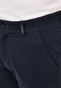 Navyblaue Hose aus Baumwollmischung. Sie verfügt über einen vorderen Knopfverschluss, schräg angenähte Seitentaschen und kontrastierende Nähte.