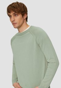 Hellgrüner Pullover mit runder Ausschnittöffnung, gerippte Ärmelbündchen und Raglanärmel, aus weichem, strukturiertem Stoff.