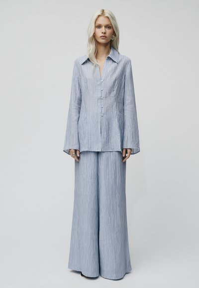Camicia button-up azzurro chiaro, con texture e maniche lunghe, abbinata a pantaloni a gamba larga dello stesso colore. Design minimalista con vestibilità rilassata.