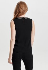 Top senza maniche nero con colletto testurizzato. Presenta una piccola apertura a occhio di chiave sul retro. Tessuto liscio e design aderente.