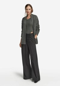 Grå stickad cardigan med ribbad textur, kombinerad med en grå figurnära topp och höga svarta vida byxor, accentuerad med eleganta svarta klackar.