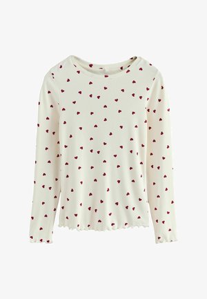 Długi rękaw bluzki w kolorze kremowym, z żebrowanym wzorem i całkowitym pokryciem małymi czerwonymi sercami. Ząbkowane wykończenie u dołu i okrągły dekolt.