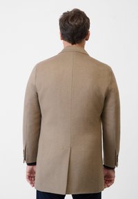 Beige ullkappa med skräddarsydd passform, slät textur, enkel ventil bak, och knäppärm, som visar minimalistiska designelement.