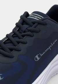 Blue athletic shoes with a smooth, textured upper, featuring dark grey laces, branded accents, and a white sole. Distinctive wave pattern design.