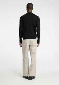 Schwarzer Strickpullover mit langen Ärmeln, kombiniert mit hellbeigen Hosen. Glatte Textur, normale Passform und seitliche Eingrifftaschen an der Hose.