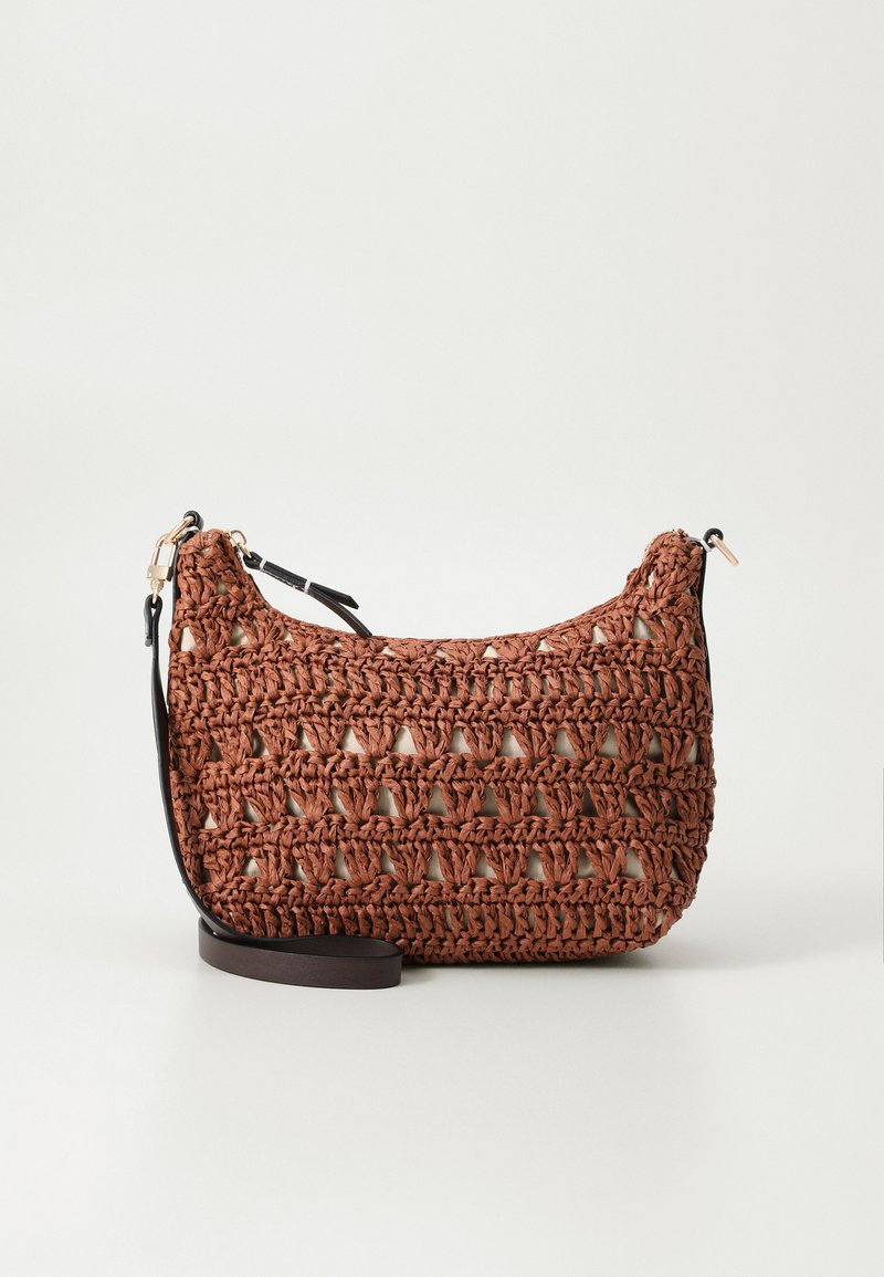 Bolso de mano de crochet marrón con forma curva, que presenta un patrón de tejido abierto y una correa negra ajustable. Cierre de cremallera en la parte superior.