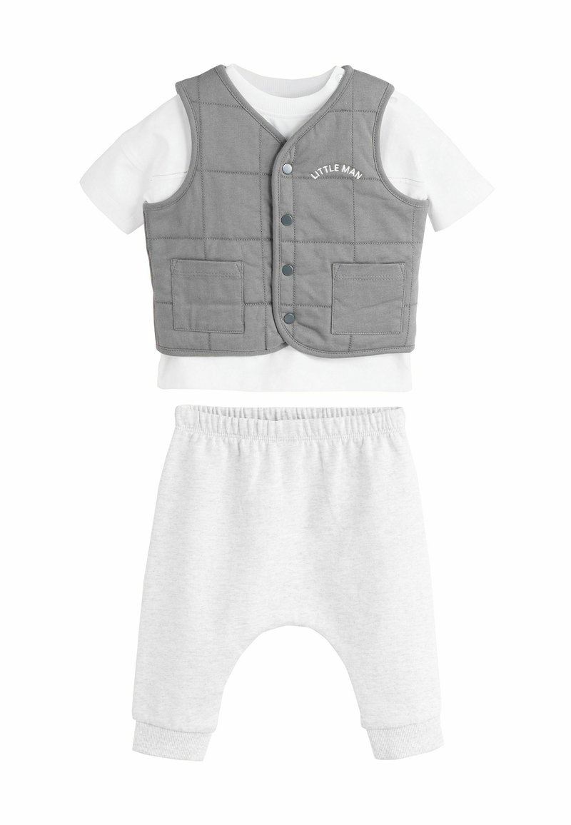 Gilet matelassé gris avec boutons et poches, chemise blanche à manches courtes en dessous, associé à un pantalon de jogging gris clair avec une taille élastique.