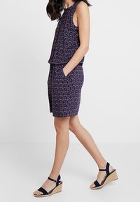 Navyblaues, ärmelloses Kleid mit floralem Muster, gerafftem Rundhalsausschnitt und lockerer Passform, kombiniert mit navyblauen Wedge-Sandalen und einer geflochtenen Plattform.