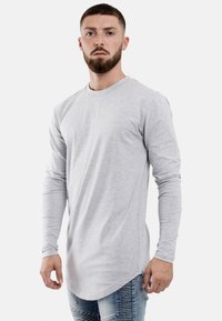 Hellgraues Langarmshirt aus weichem Material mit Rundhalsausschnitt und abgerundetem Saum. Kombiniert mit lässigen blauen Jeans.