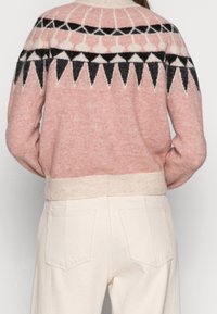 Rosa Strickpullover mit geometrischem Muster in Schwarz und Creme. Mit geripptem Saum und Bündchen sowie einer weichen, strukturierten Oberfläche.