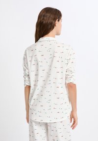 Witte langefsleevenshirt met een zachte textuur, voorzien van een meerkleurig patroon van kleine huisjes en bomen over de stof.