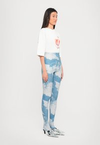 Camiseta blanca con un diseño gráfico rojo, combinada con leggings azules que presentan un patrón de nubes, y mulas plateadas brillantes en los pies.