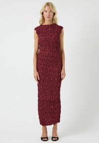 Burgunderfarget ermeløs kjole med strukturert blomsterm�ønster, knelang, tettsittende silhuett og subtil rysjekant rundt halsen, kombinert med svarte høyhælte sko.