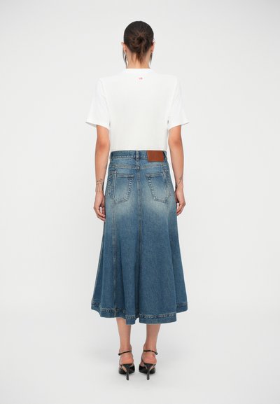 Tricou alb scurt cu logo roșu, asortat cu o fustă din denim, de lungime medie, de culoare albastră, cu accente estompate și margine netă. Sandale negre cu curele.