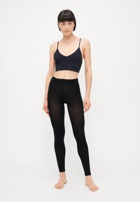 Svart sømløs crop top kombinert med svarte leggings. Stoffet er glatt og elastisk, med høy midje og et minimalistisk design.