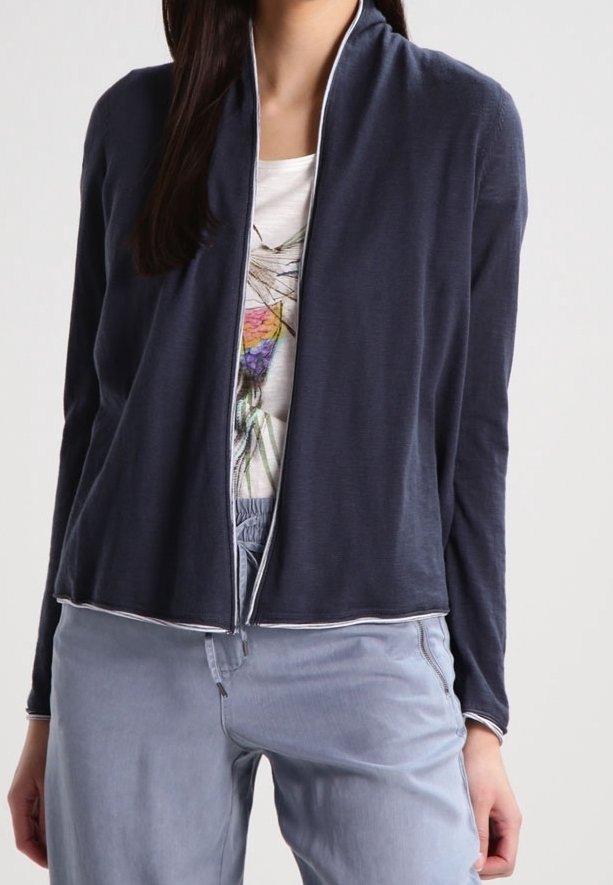 Femme portant un cardigan bleu foncé ouvert sur un t-shirt blanc avec un motif graphique et un pantalon bleu clair.