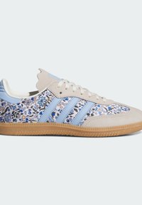 Sneaker mit floralem Muster in Blau und Weiß, mit oberem Teil aus hellgrauem Wildleder, blauen Akzenten, zwei blauen Streifen und Sohle aus Gummigummi.