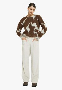 Maglione marrone e bianco con motivo a fantasia, bordi a coste ai polsini e all'orlo, abbinato a pantaloni larghi di velluto a coste beige chiaro e scarpe marroni.