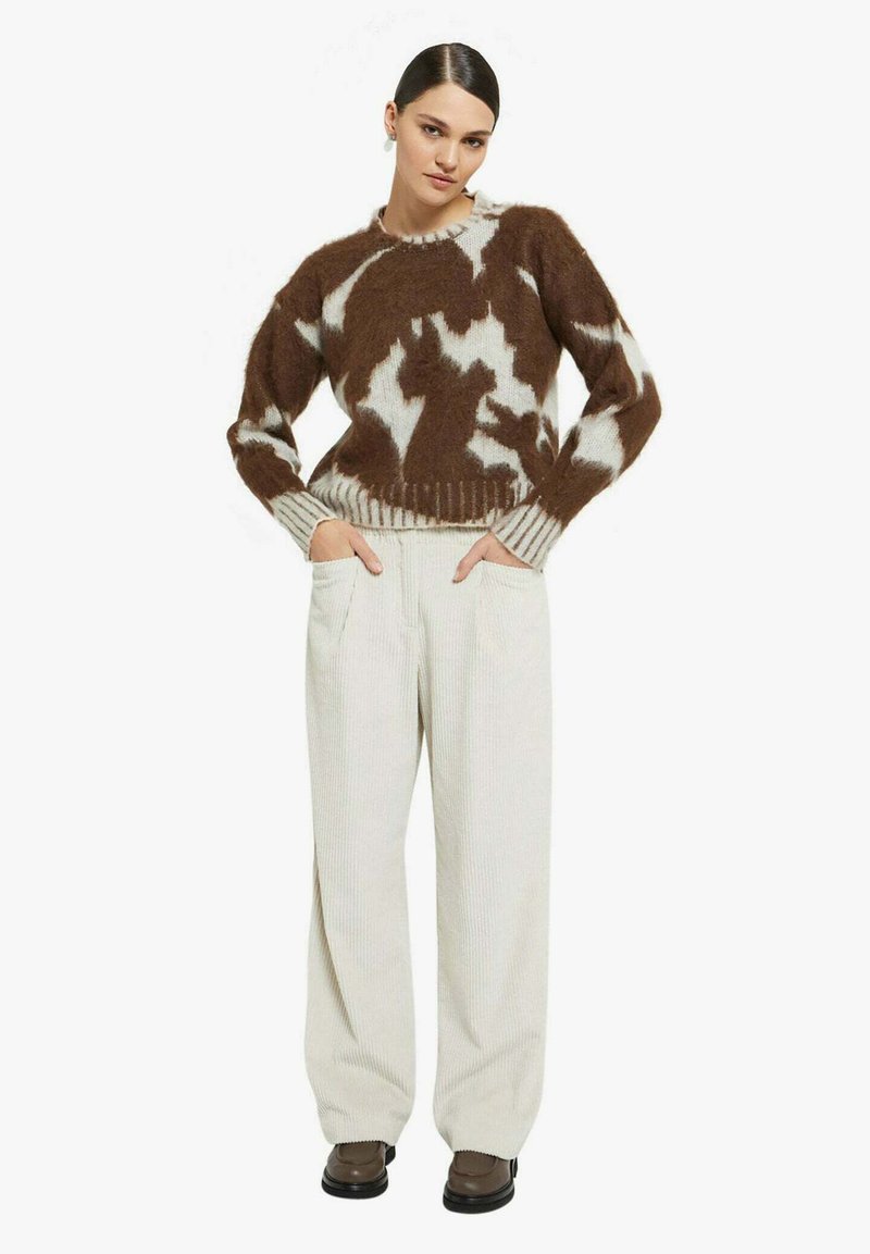 Maglione marrone e bianco con motivo a fantasia, bordi a coste ai polsini e all'orlo, abbinato a pantaloni larghi di velluto a coste beige chiaro e scarpe marroni.