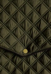 Tkanina w kolorze oliwkowym o pikowanym wzorze w diamenty. Posiada złoty zatrzask na górze oraz kontrastujące czarne przeszycia wzdłuż krawędzi.