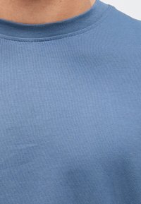 Svetlo modra majica s kratkimi rokavi, z okroglim izrezom, izdelana iz gladke mešanice bombaža, z drobno rebrasto teksturo okoli izreza.