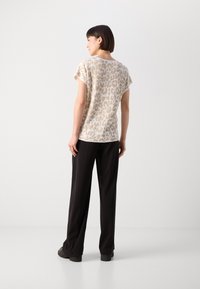 T-shirt beige à manches courtes avec un motif léopard, associé à un pantalon noir à jambes larges. Texture lisse et coupe décontractée.
