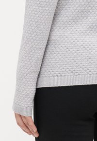 Pulover gri deschis cu un model texturat de fagure, cu manșete și tiv cu nervuri, asortat cu pantaloni negri. Design casual și textură a materialului vizibile.