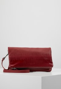 Červená kožená kabelka přes rameno s texturovaným povrchem, překlopným víkem a odnímatelným popruhem; obsahuje stříbrný zip a detail s logem.