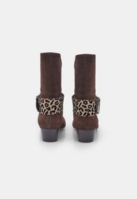 Bottes ankle en suède brun avec une bande en imprimé léopard et des détails de boucle. Talons carrés offrant de la stabilité ; conçues pour le confort et le soutien.