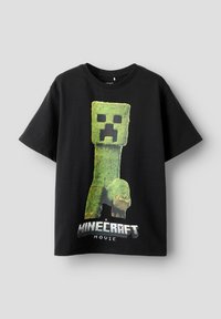 Svart bomulls t-shirt med en grön blockfigurdesign, med "Minecraft Movie" tryckt i fet vita bokstäver längst ner.