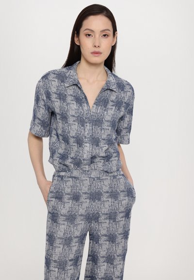 Mönstrad tvådelad outfit i nyanser av blått och vitt; kortärmad button-up topp med krage och matchande högmidjade byxor, båda med texturerad design.