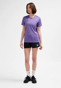 Lila sporttröja med korta ärmar, kombinerad med svarta shorts. Har en diskret logotyp och kontrasterande material. Vita strumpor och svarta skor.