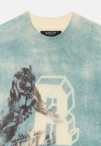 Maglione lavorato a maglia in un morbido blu chiaro e crema, con una grafica di un orsacchiotto e la lettera "R" in colori a contrasto. Collo rotondo, tessuto testurizzato.