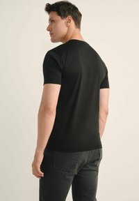 Czarny t-shirt z krótkim rękawem, wykonany z gładkiego materiału, z klasycznym okrągłym dekoltem i dopasowanym krojem, noszony z ciemnoszarymi dżinsami.