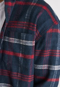 Mörkblå rutig skjorta med röda och vita ränder, tillverkad av mjuk flanell, med en ficka i lappstil och detaljerad krage med knäppning.