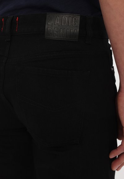 Fekete farmernadrág, textúrált felülettel, "ZADIG DENIM" feliratos bőr derékpánttal és két hátsó zsebbel, finom varrásmintával.