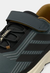 Czarno-szare buty sportowe z teksturowaną cholewką z siateczki, elastycznymi sznurówkami, rzepem oraz beżową podeszwą z czarnymi akcentami.