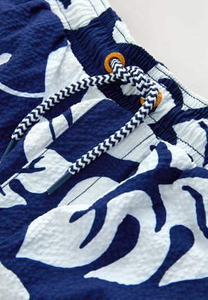 Mėlyni ir balti plaukimo šortai su raštais, pagaminti iš tekstūruotos medžiagos. Turi elastinę juostą liemens srityje su tamsiai mėlyna ir balta raišteliu bei oranžiniais akcentais.