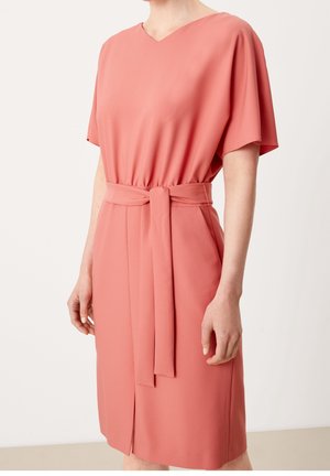 Korálově růžové šaty vyrobené z hladkého materiálu, s výstřihem do V, krátkými rukávy, zavazováním v pase a předním rozparkem pro snadný pohyb.