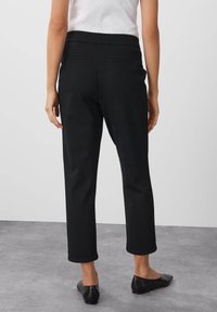 Svarta, vävda byxor med rak ben, elastisk midja och två bakfickor, stylade med svarta, platta skor.