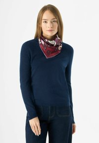 Marineblauwe trui van zacht materiaal, gecombineerd met een geborduurde bordeauxrode zijden sjaal die om de hals is gestrikt, wat het detail en de textuur van de outfit versterkt.